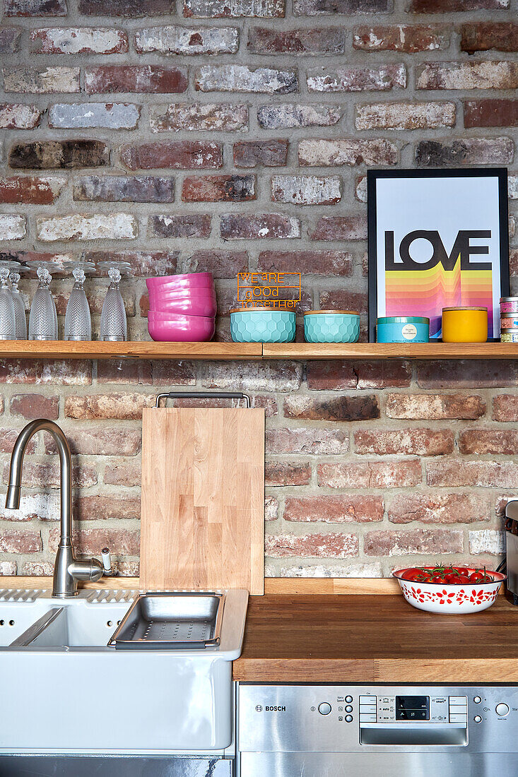 Kitchen corner with open shelf on brick wall and colourful decorative elements