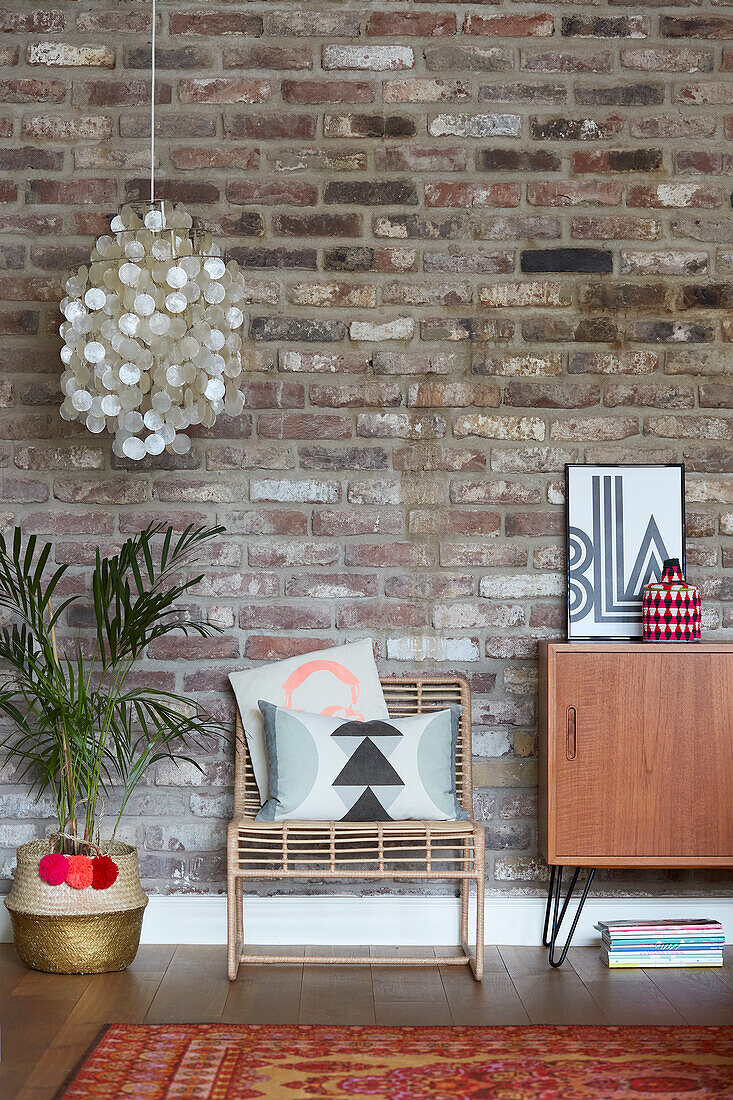 Chair next to mid-century cabinet in front of brick wall and shell lamp