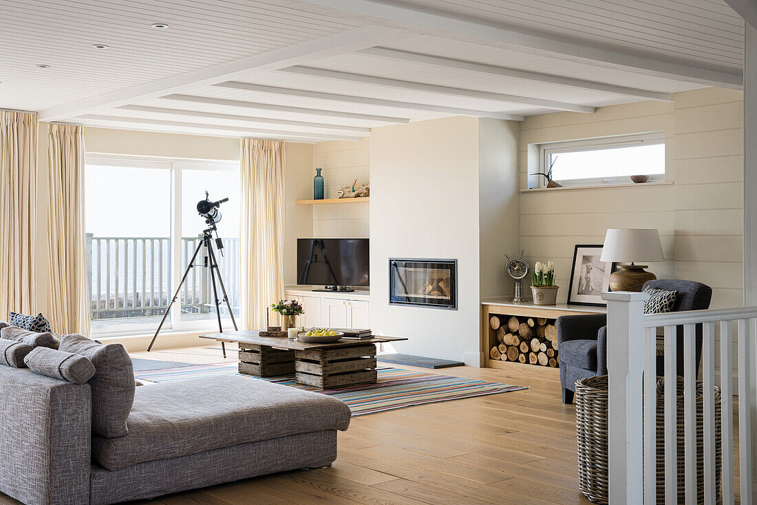 Light-flooded living room with grey sofa and fireplace, telescope in front of the balcony