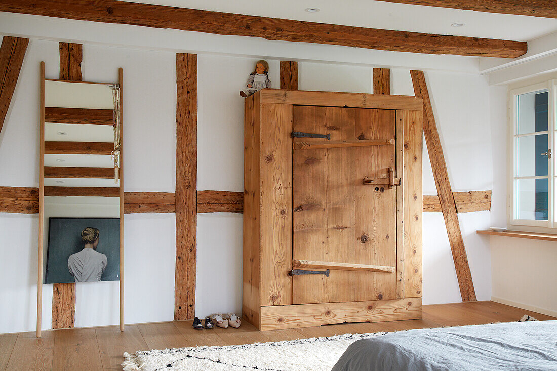 Holzschrank und Spiegel in rustikalem Schlafzimmer mit Sichtbalken