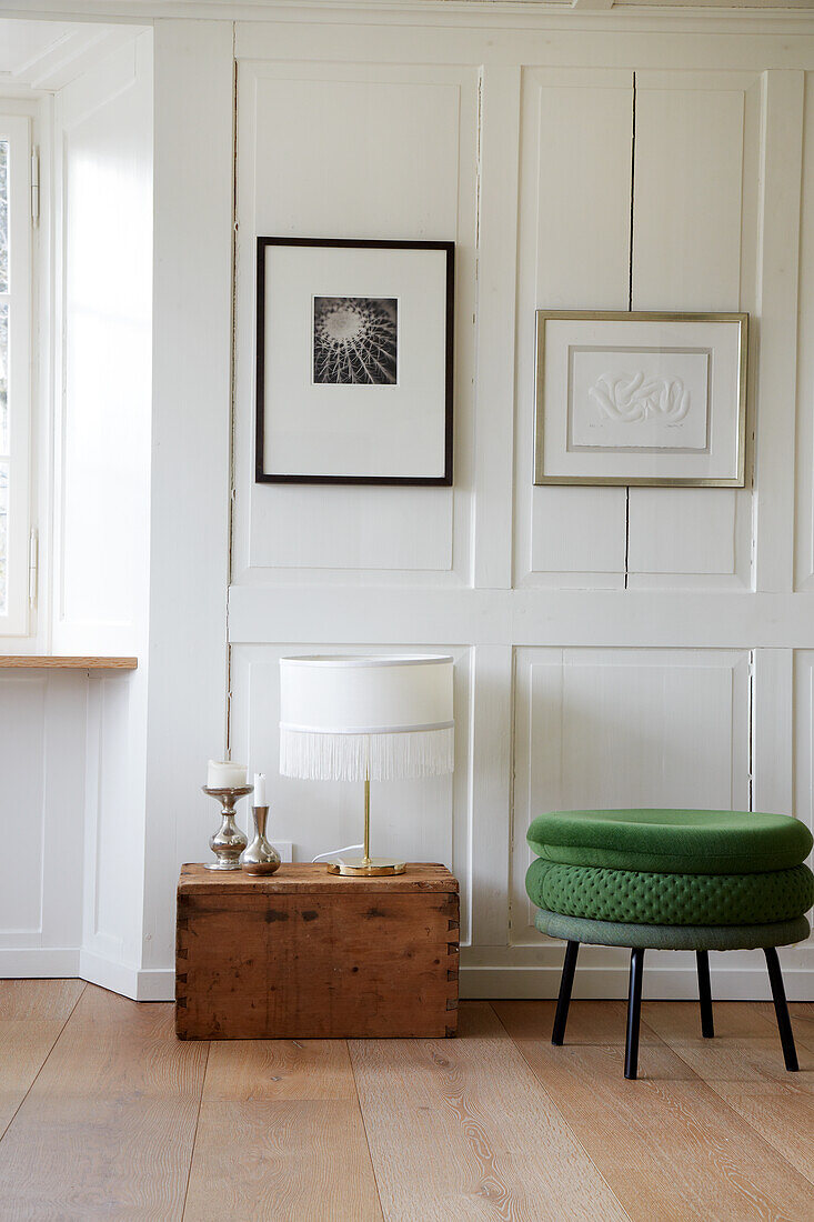 Old wooden chest with table lamp and green stool in front of wall with white wood panelling