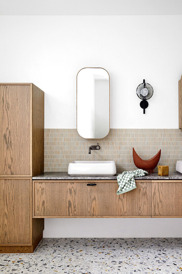 Bathroom vanity with wooden cabinet fronts in bathroom with terrazzo floor