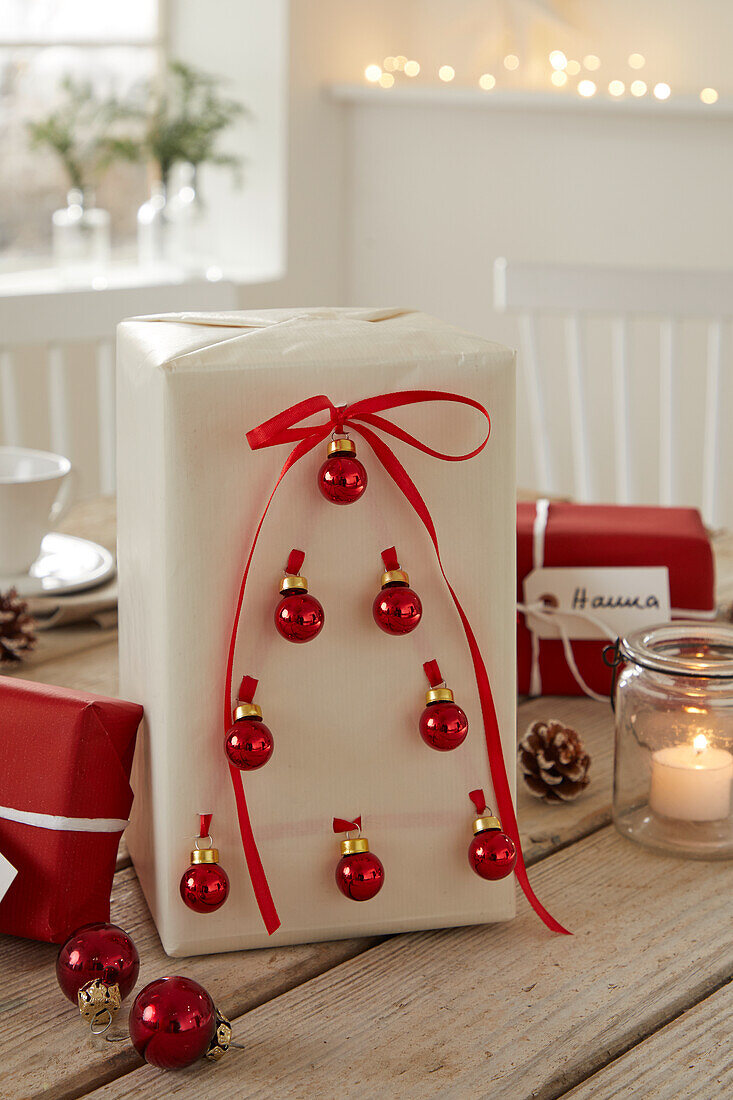 Wrapped gift with red bow and small Christmas baubles on wooden table