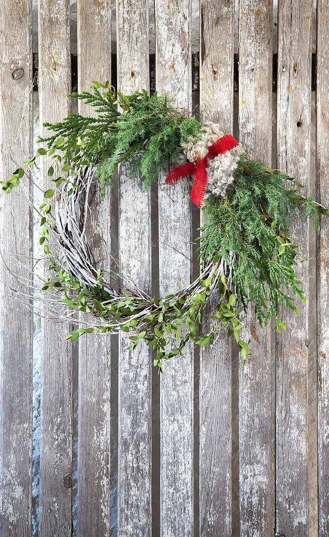 Weihnachtlicher Kranz an Holzwand mit rotem Band und Tannengrün