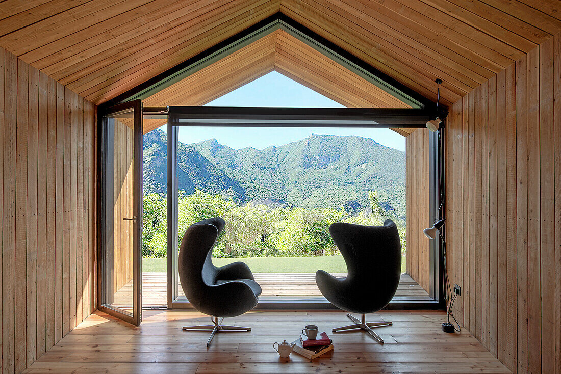 Holzinterieur mit Designersesseln und Panoramafenster mit Bergblick