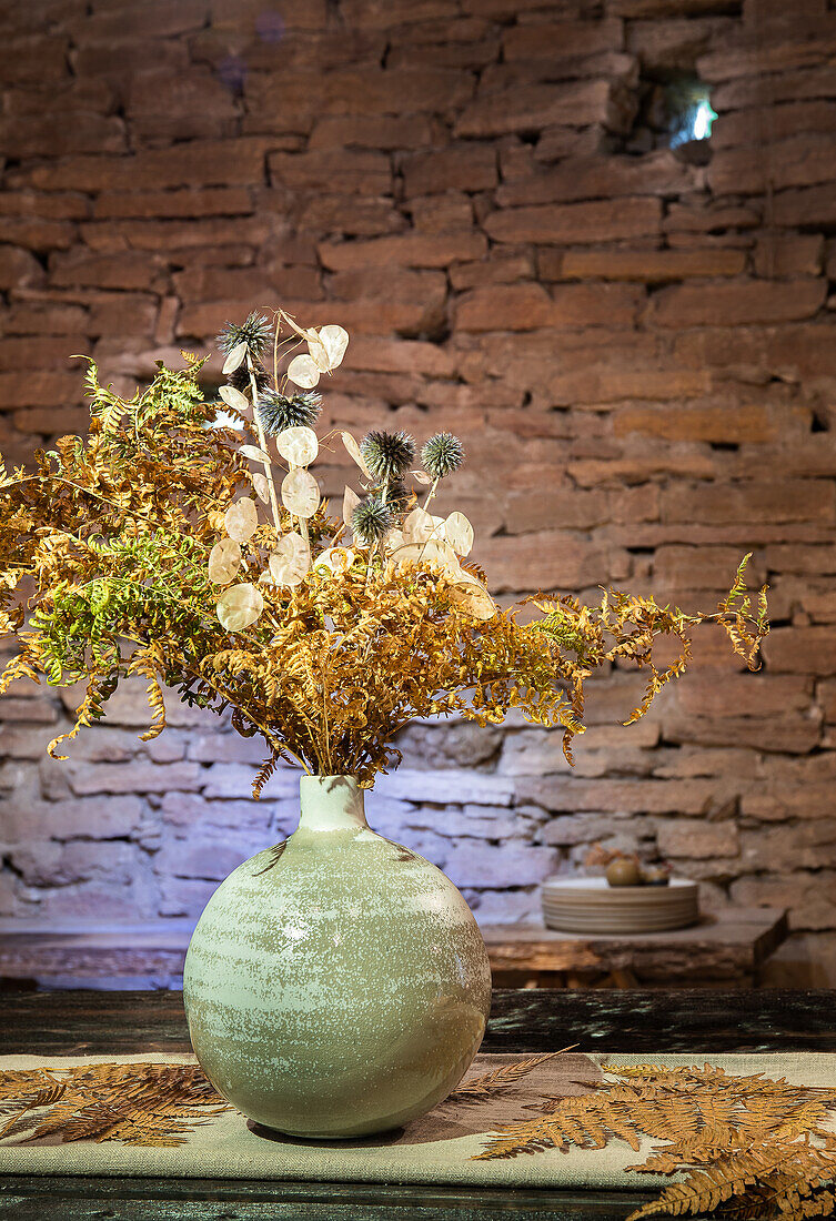 Dried flower arrangement in ceramic vase in front of rustic brick wall