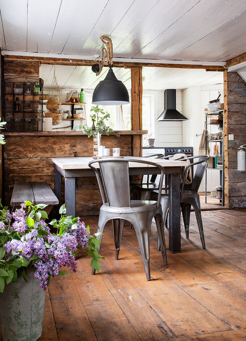 Country-style kitchen with metal chairs and wooden table, lilac branches in floor vase