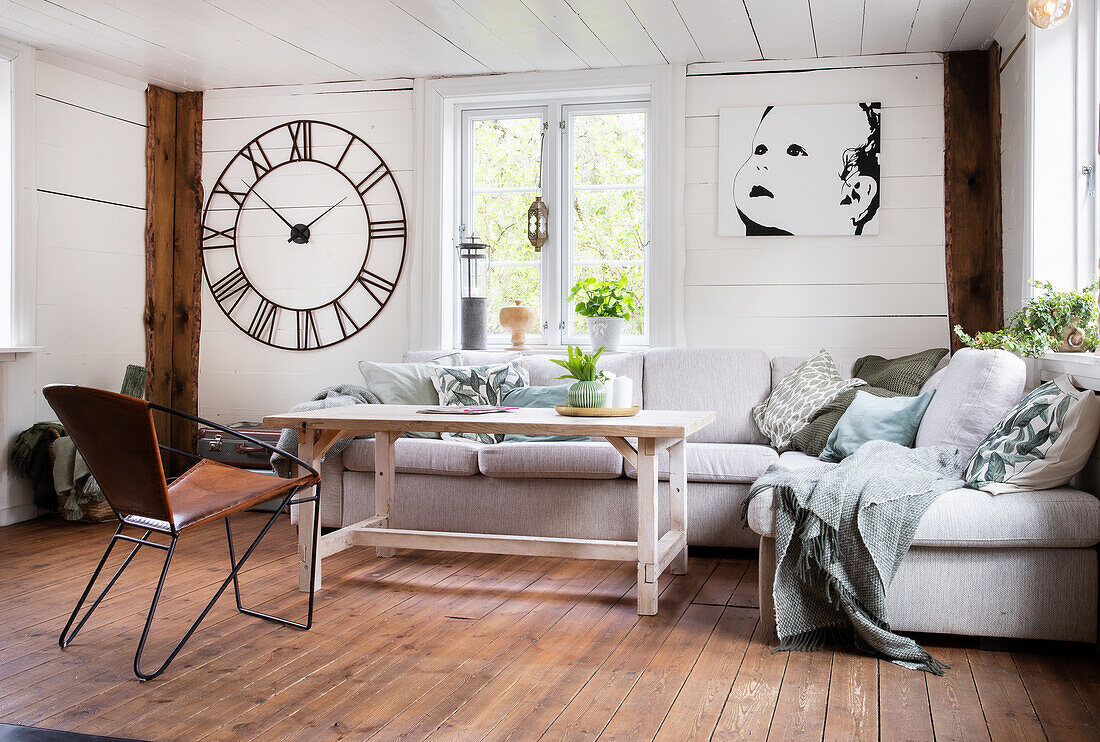 Helles Wohnzimmer mit großer Wanduhr, Sofa, Couchtisch aus Holz und Bild an der Wand
