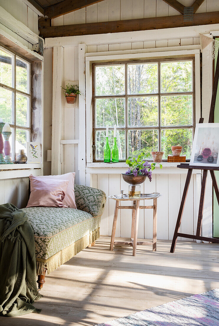 Light-coloured garden shed with daybed and easel, rustic ambience