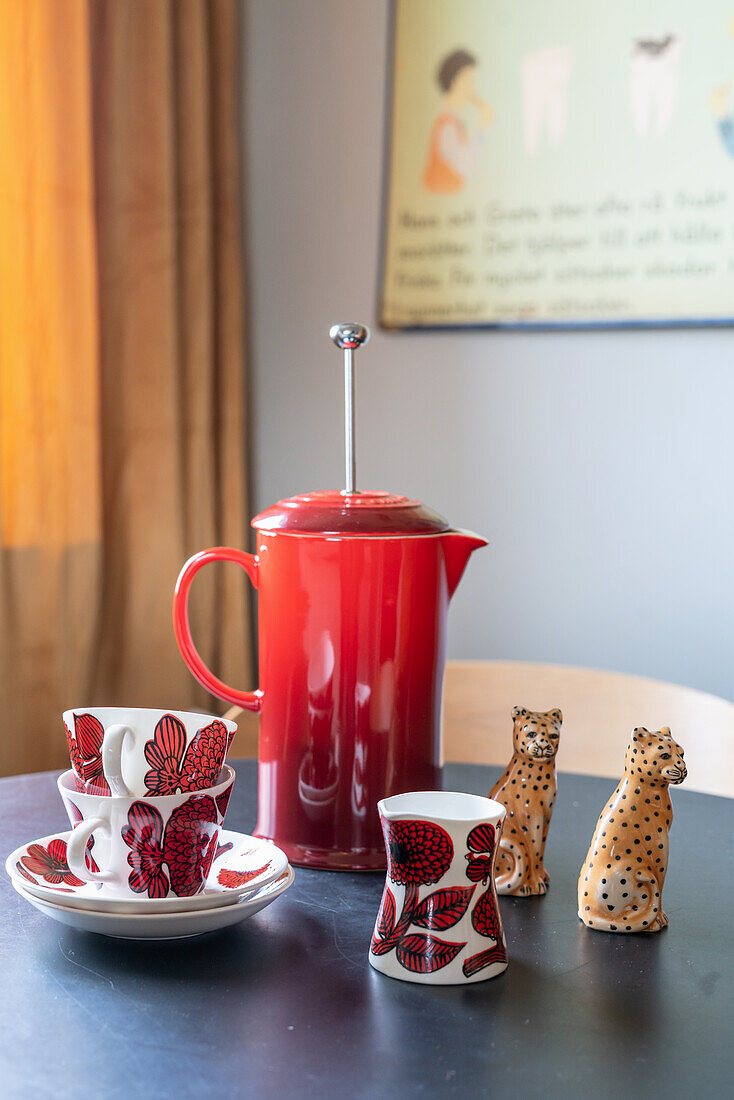Cups, a red coffee pot and salt and pepper shakers on a breakfast table