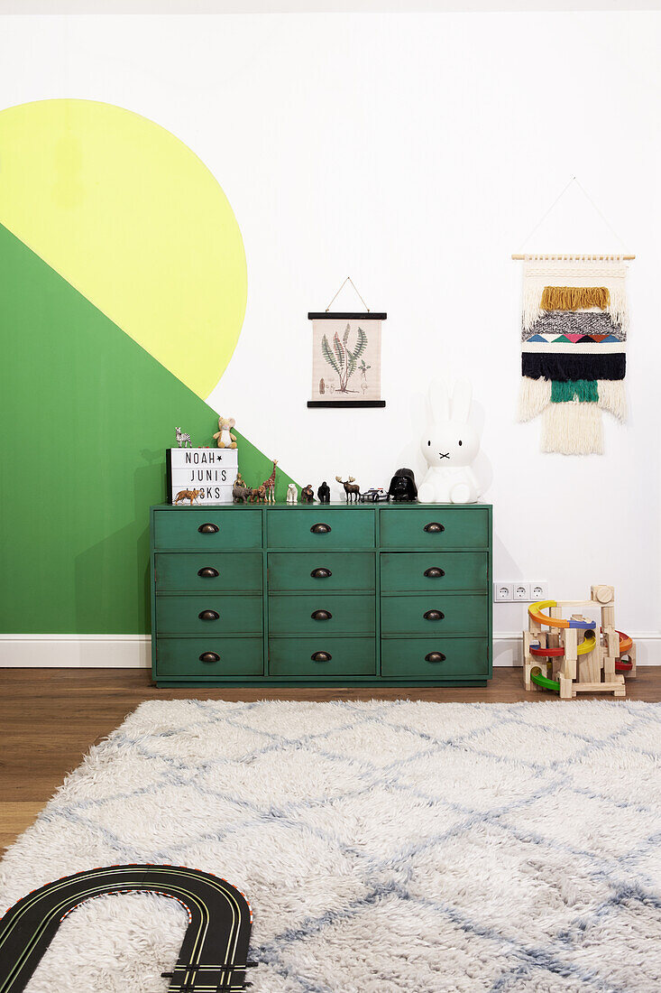 Dark green chest of drawers in children's room with toys and wall decorations