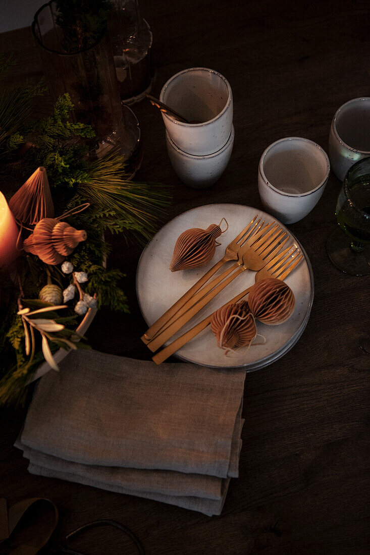 Festlich gedeckter Holztisch mit goldfarbenem Besteck und Papierornamenten