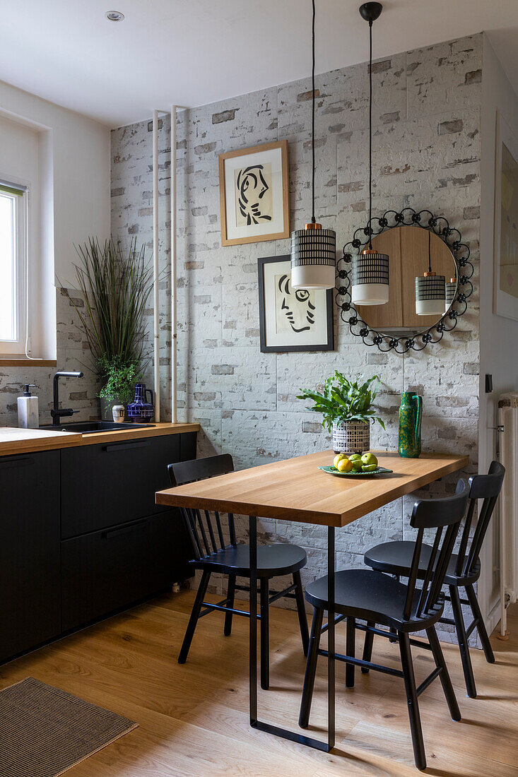Küchenunterschrank mit schwarzer Front und Esstisch mit Stühlen, darüber Pendelleuchten