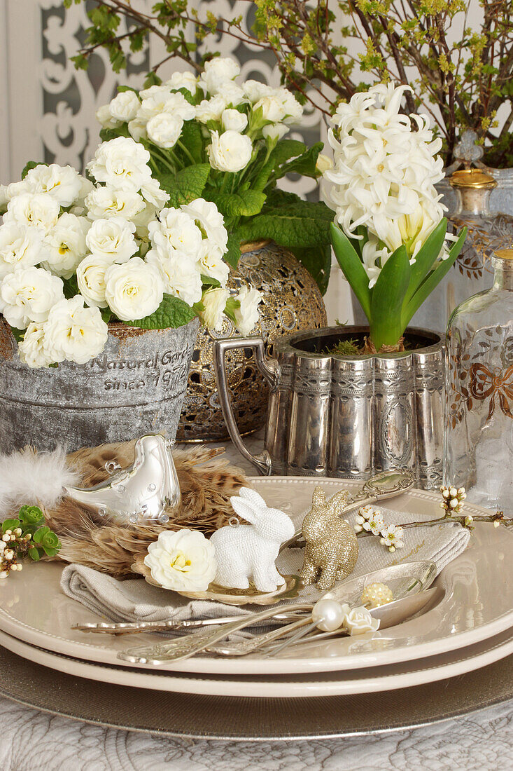 Ostergedeck mit Silberbesteck und Hasenfiguren, weiße Primeln und Hyazinthen auf Tisch