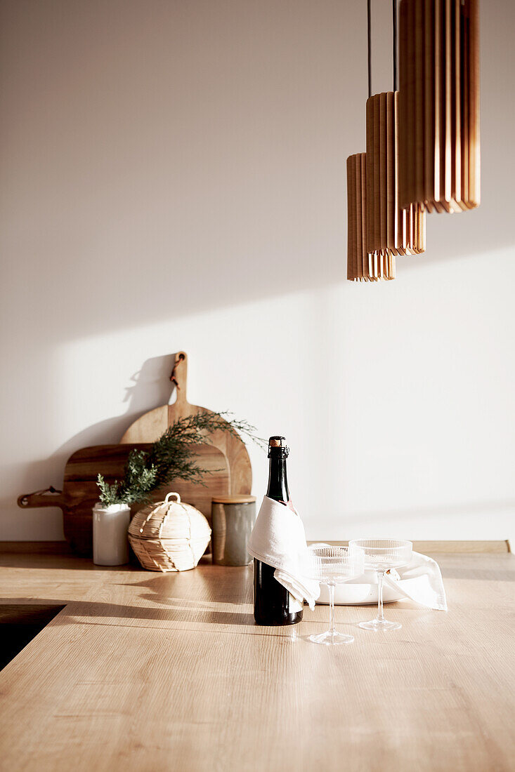 Champagne bottle and glasses on a wooden countertop, pendant lights above