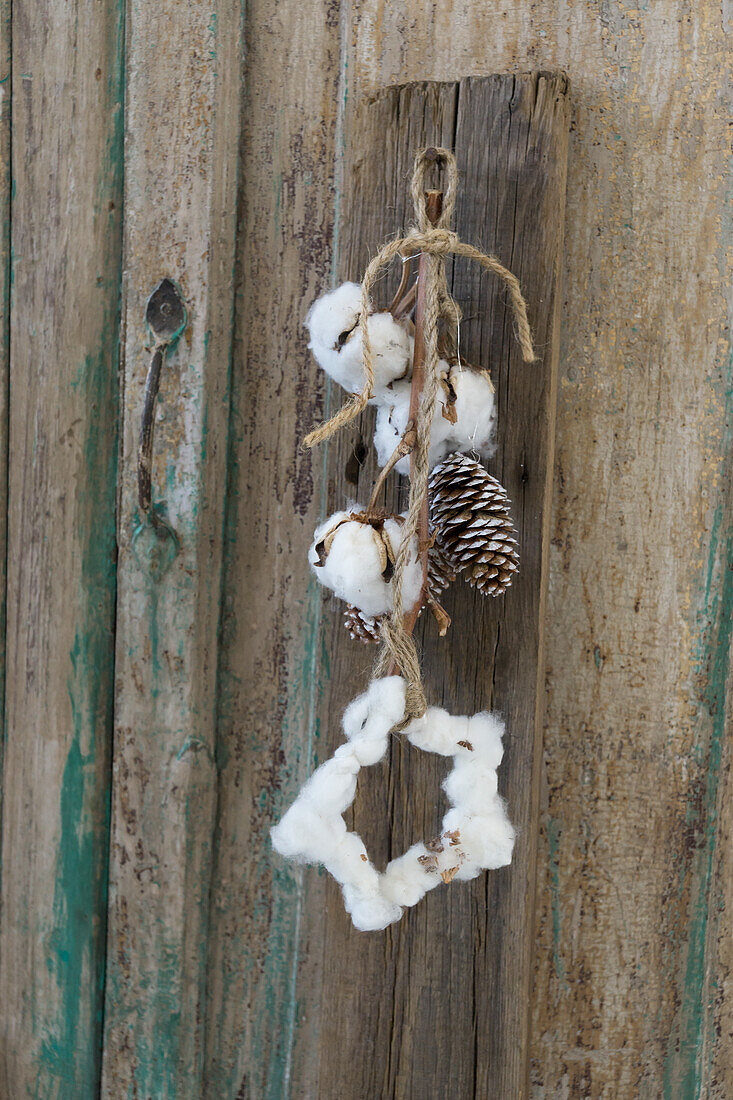 Garland with star of cotton and whitewashed pine cones hanging on an old cupboard door