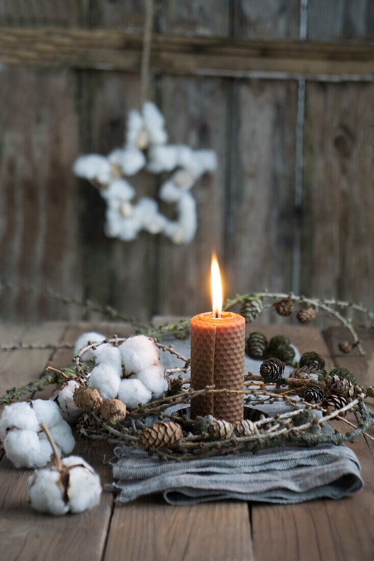 Rolled beeswax candle with a wreath of larch cones and cotton on a linen cloth