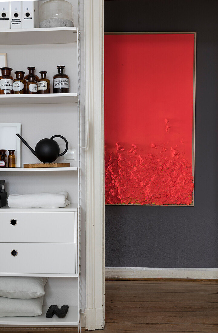 Apothecary shelves by the doorway with a view of red artwork on black wall
