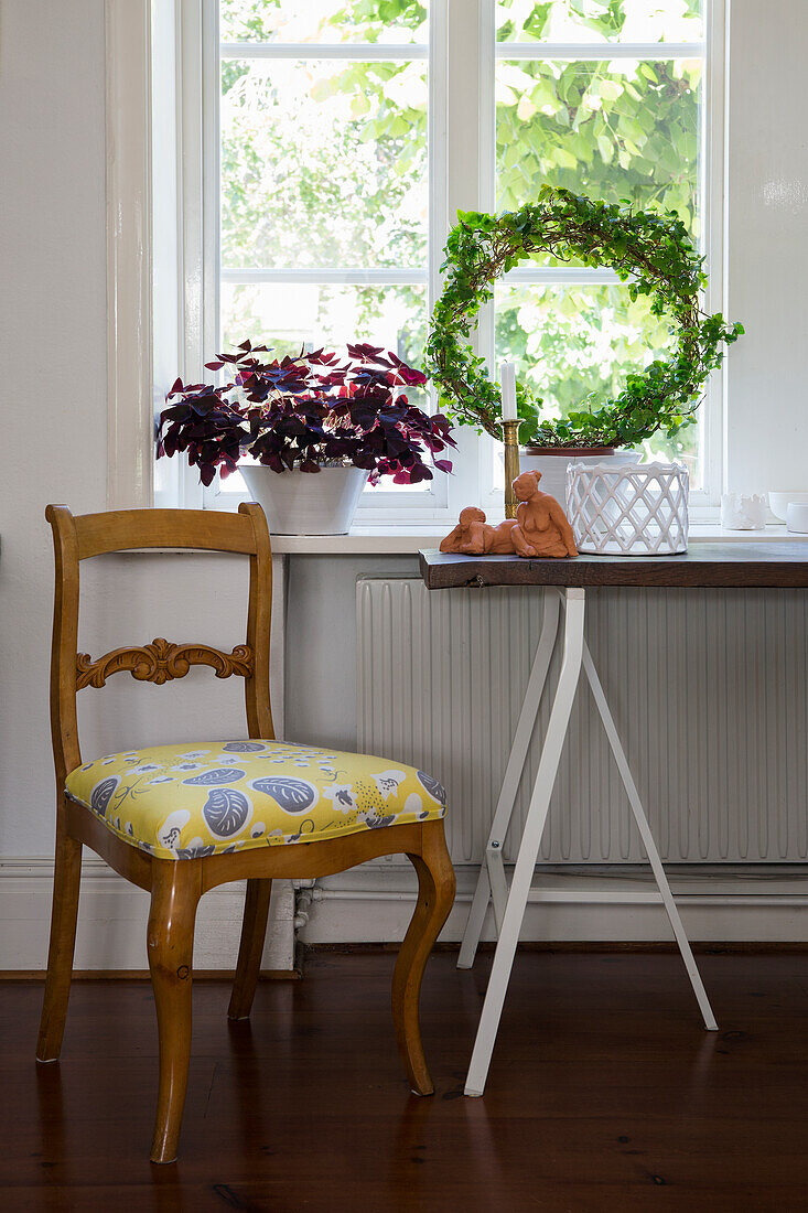 Alter Stuhl mit neuer Polsterung, Tisch aus Eichenbrett auf Böcken vor Fenster mit Zimmerpflanzen
