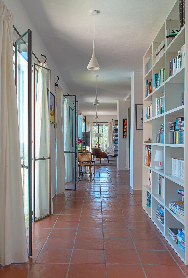 Hallway with French doors and bookshelf in Mediterranean house with terracotta tile floor