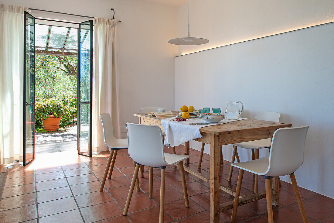 Rustikaler Esstisch aus Holz mit weißen Stühlen in mediterranem Zimmer mit Terrakottafliesenboden