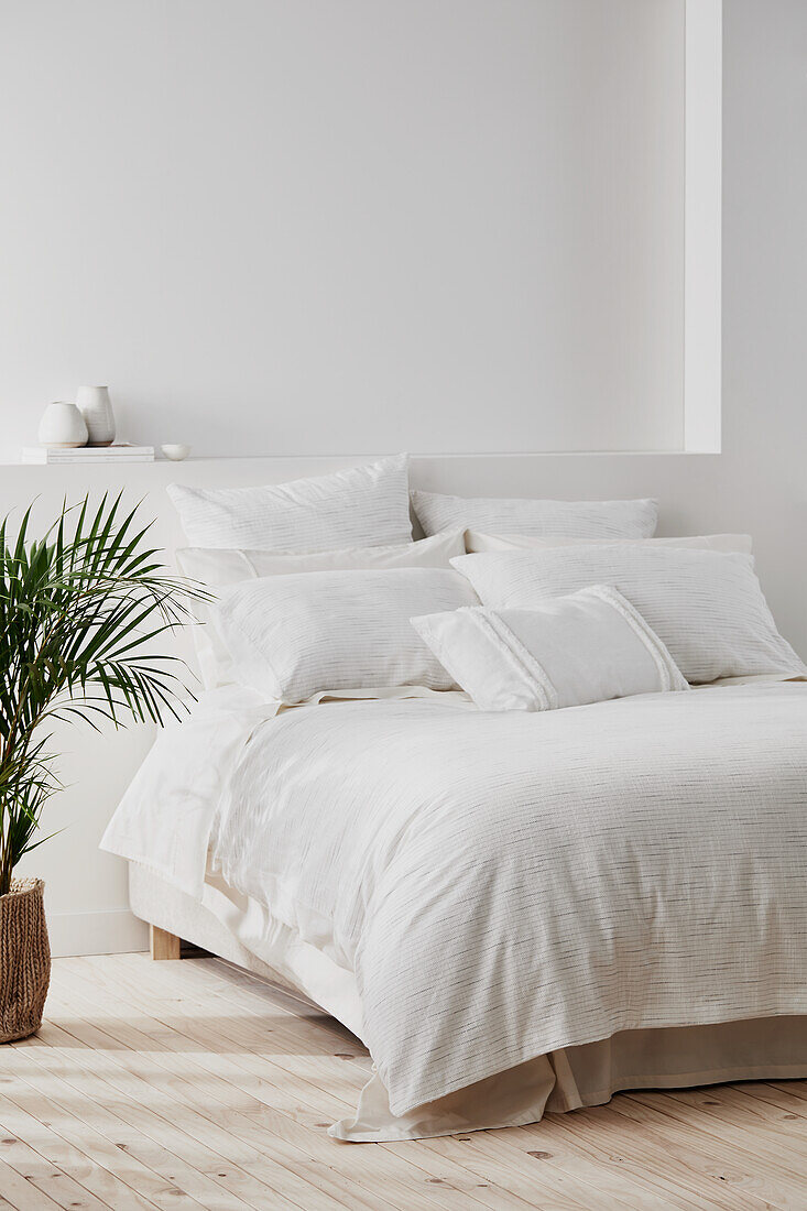 Schlafzimmer im Küstenstil mit weißen Wänden, weißer Bettwäsche und einer Topfpalme