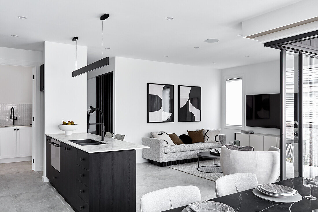 A living room with a grey sofa and abstract art next to an open-plan kitchen with a small laundry room in the background