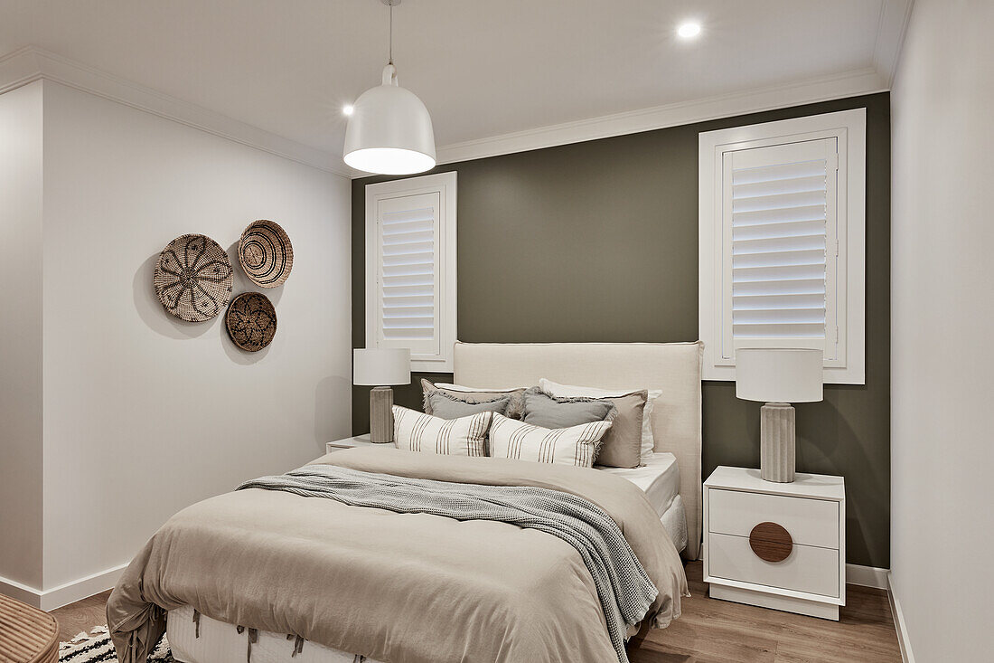 A coastal style bedroom with beige linen bedding, an olive feature wall and woven ethnic baskets on the wall