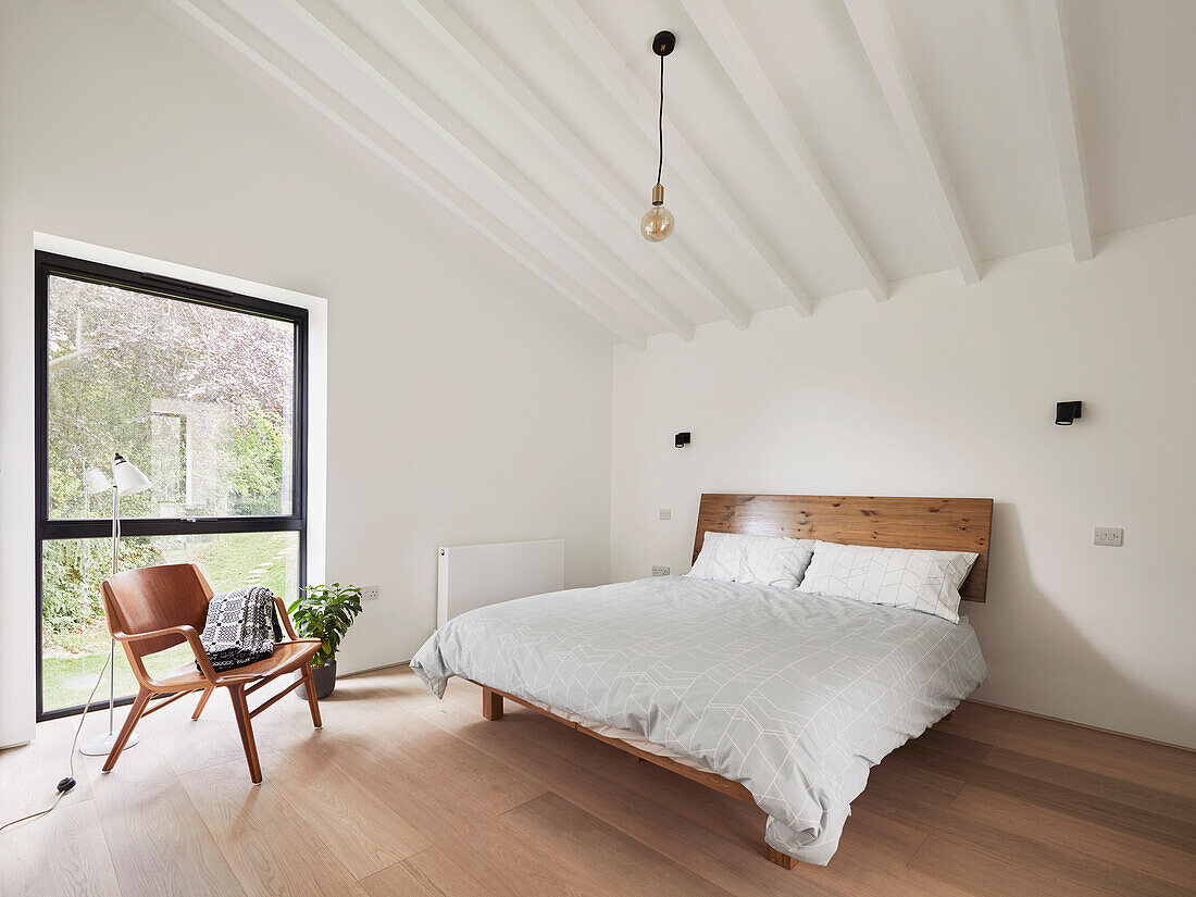 A wooden bed and a chair in a simple bedroom with a high ceiling