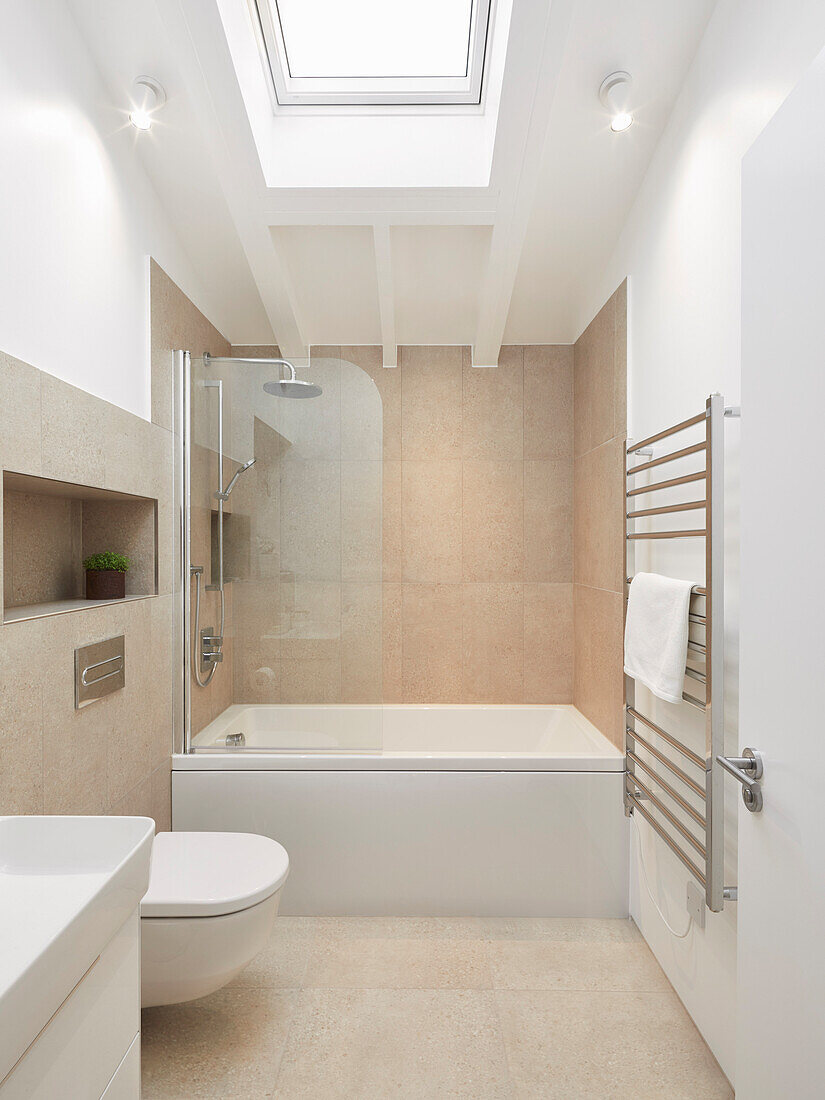 A small, modern bathroom in beige and white with a skylight