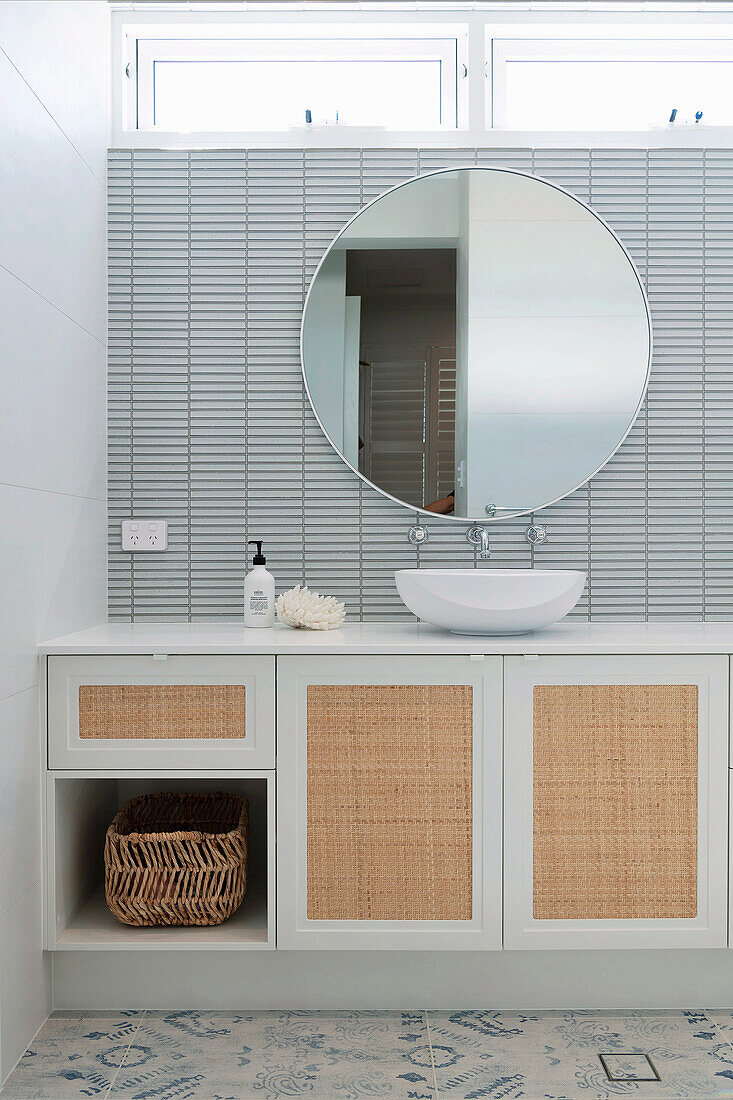Vanity unit with a woven cane inlay and large, round wall mirror in the bathroom