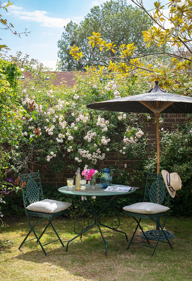Charmanter Sitzplatz mit Sonnenschirm vor blühenden Rosen im Garten