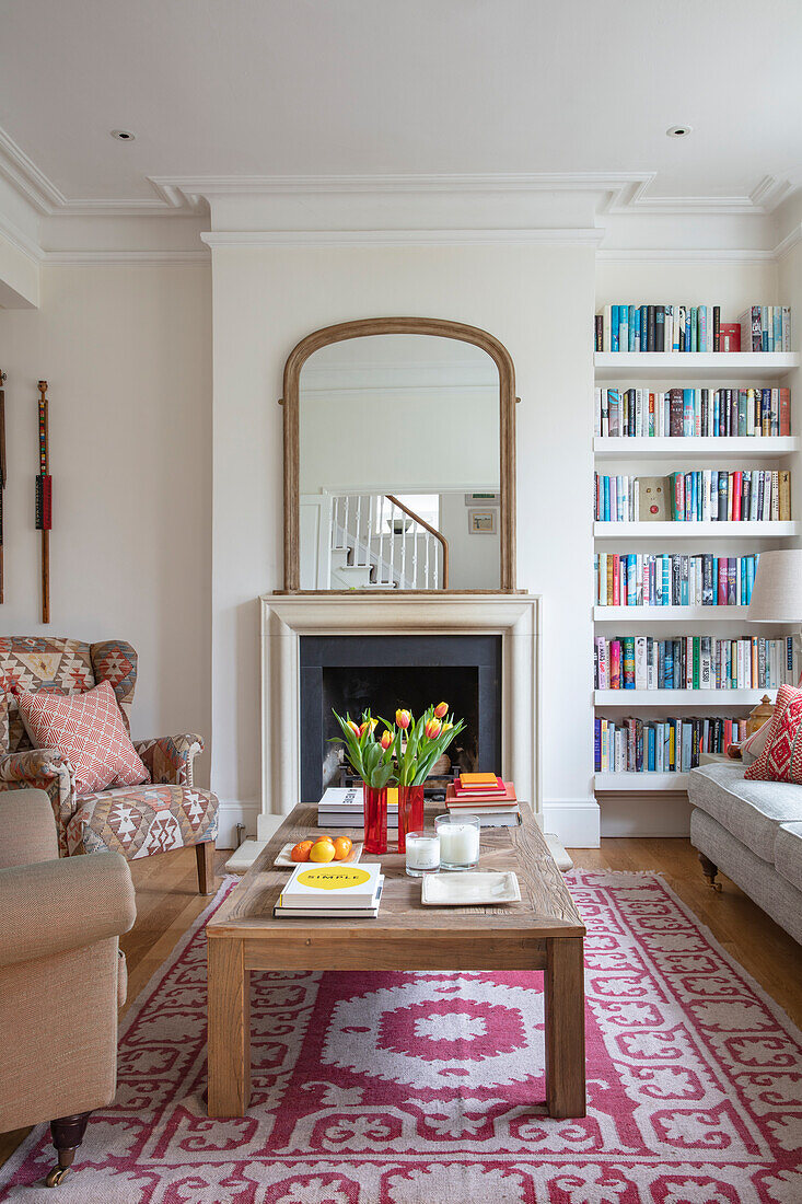 Blick über Couchtisch aus Holz auf Kamin mit Spiegel, daneben Bücherregal im Wohnzimmer
