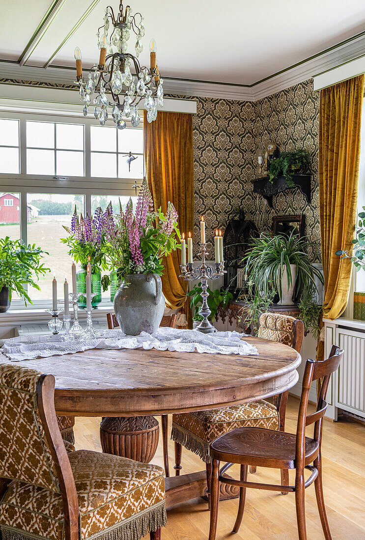 Round dining table with bouquet of flowers in a rural room with wallpaper