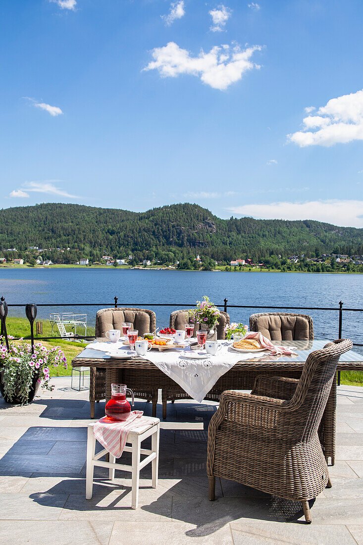 Set table and rattan armchairs on sunny terrace with a lake view