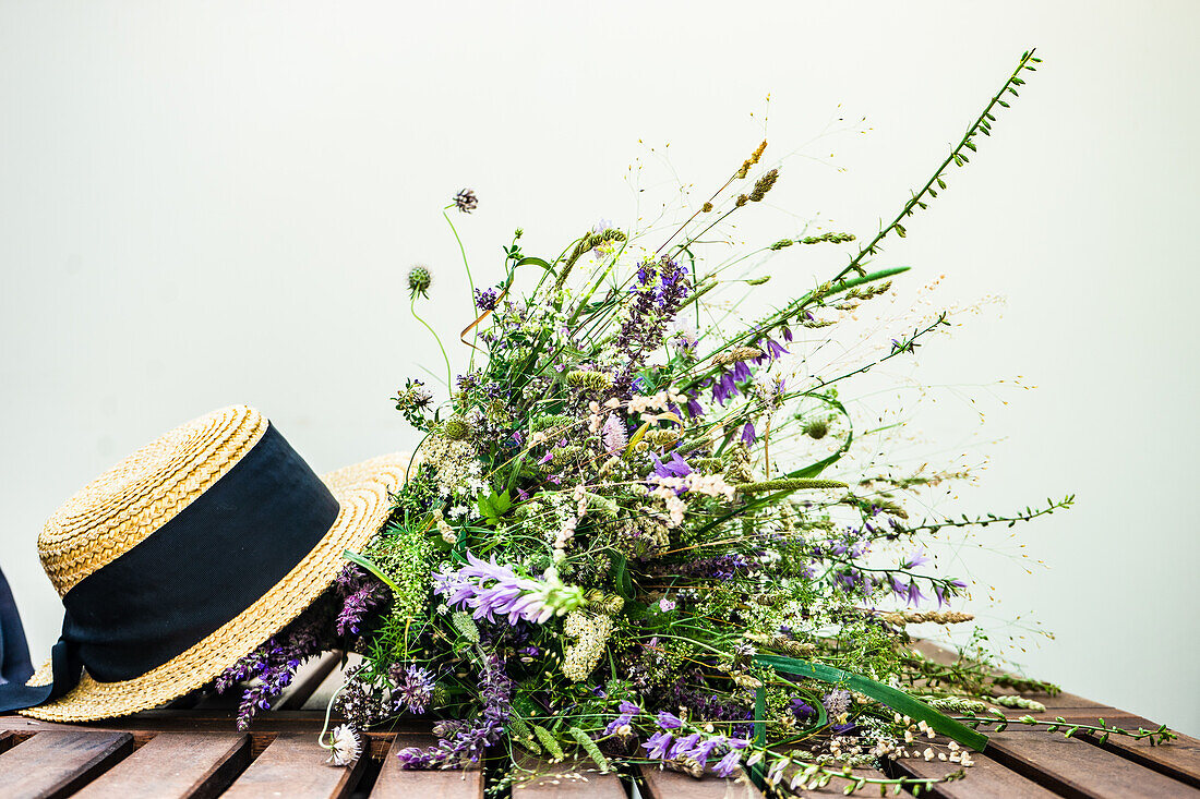 Wildblumen in Blumenstrauß und Strohhut auf Holztisch