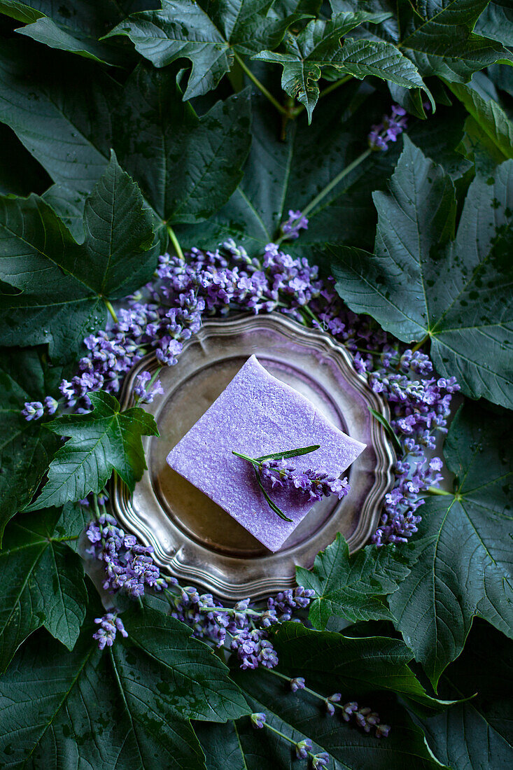 Natural lavender soap on silver tray surrounded by flowers and leaves