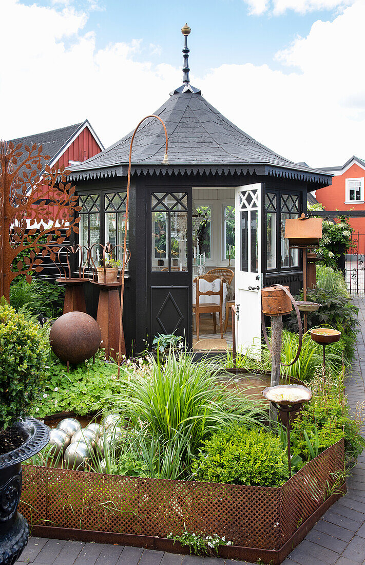 Black painted gazebo and small flower bed with rusty fence