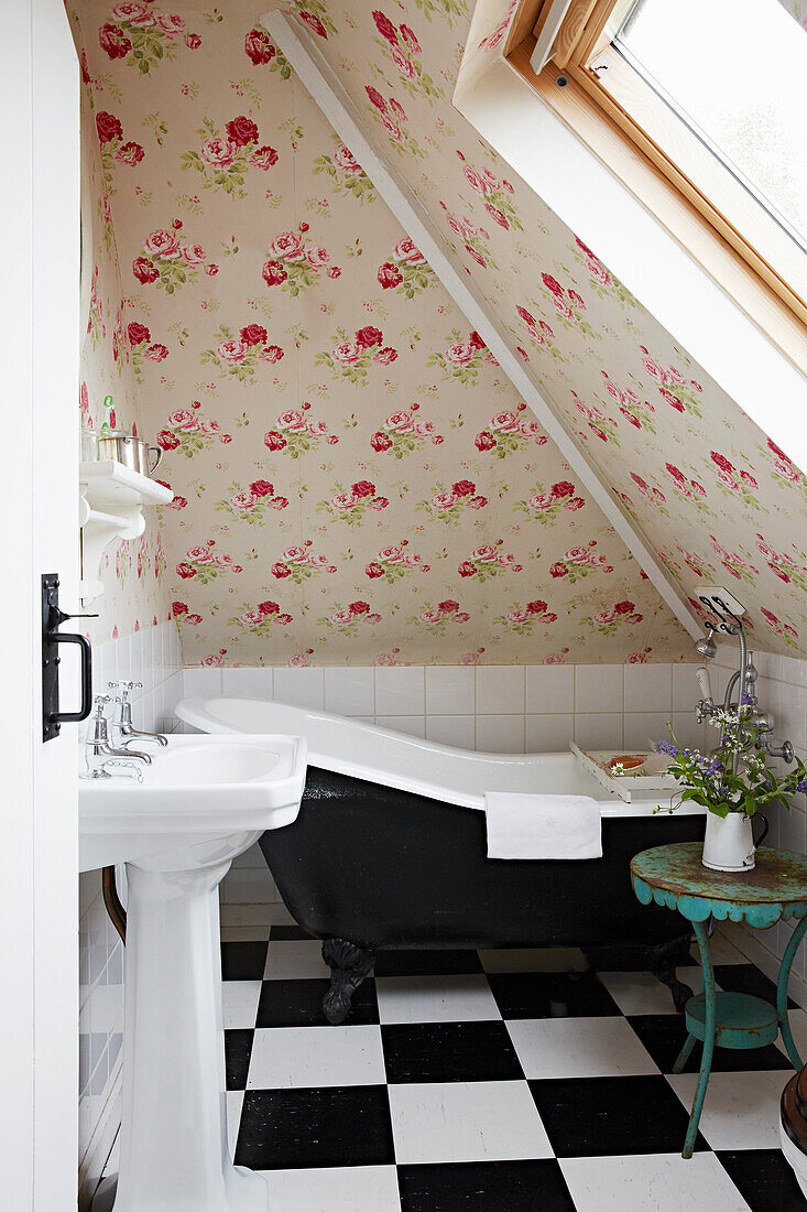 Black and white freestanding bathtub in the attic room with floral wallpaper