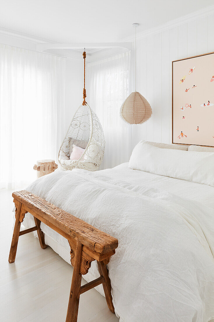 Bett mit weißer Bettwäsche, Bank aus indischem Holz und Hängesessel im Schlafzimmer