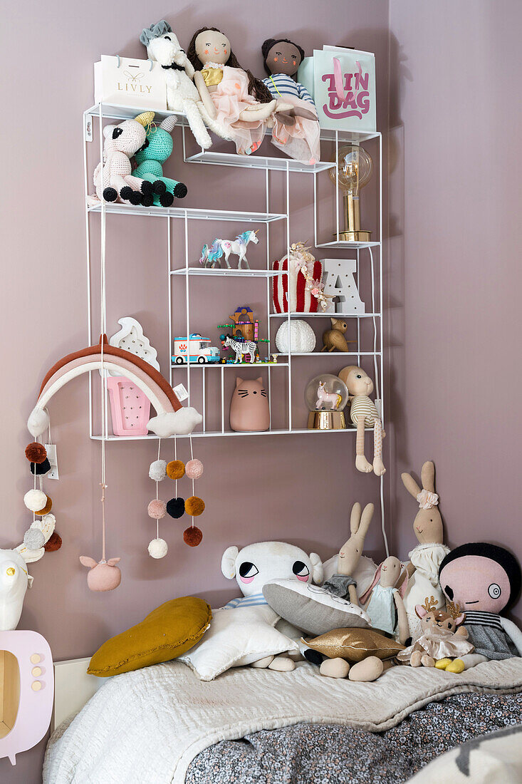 Wandregal mit Puppen und Dekoobjekten über Kinderbett mit Kuscheltieren
