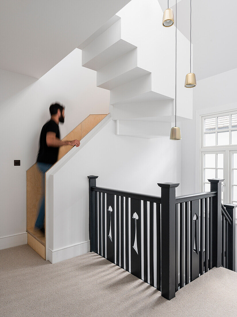 Weißes Treppenhaus mit schwarzem Geländer, Mann auf der Treppe