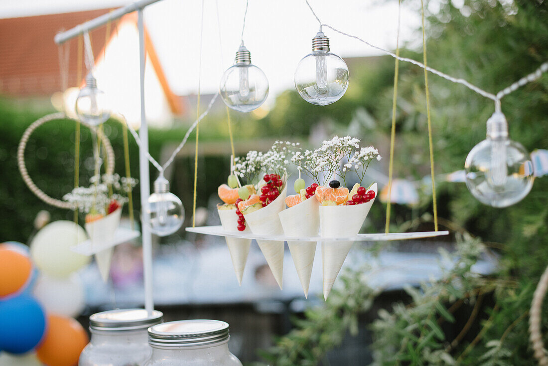 Fruit in paper cones on a hanging shelf, surrounded by fairy lights
