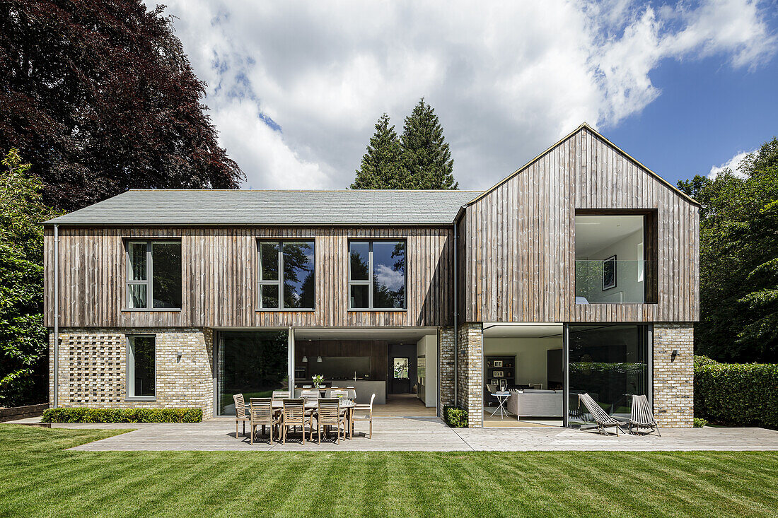 Neubauhaus mit Fassade aus Ziegelsteinen und Holzverkleidung, sonnige Terrasse mit Esstisch