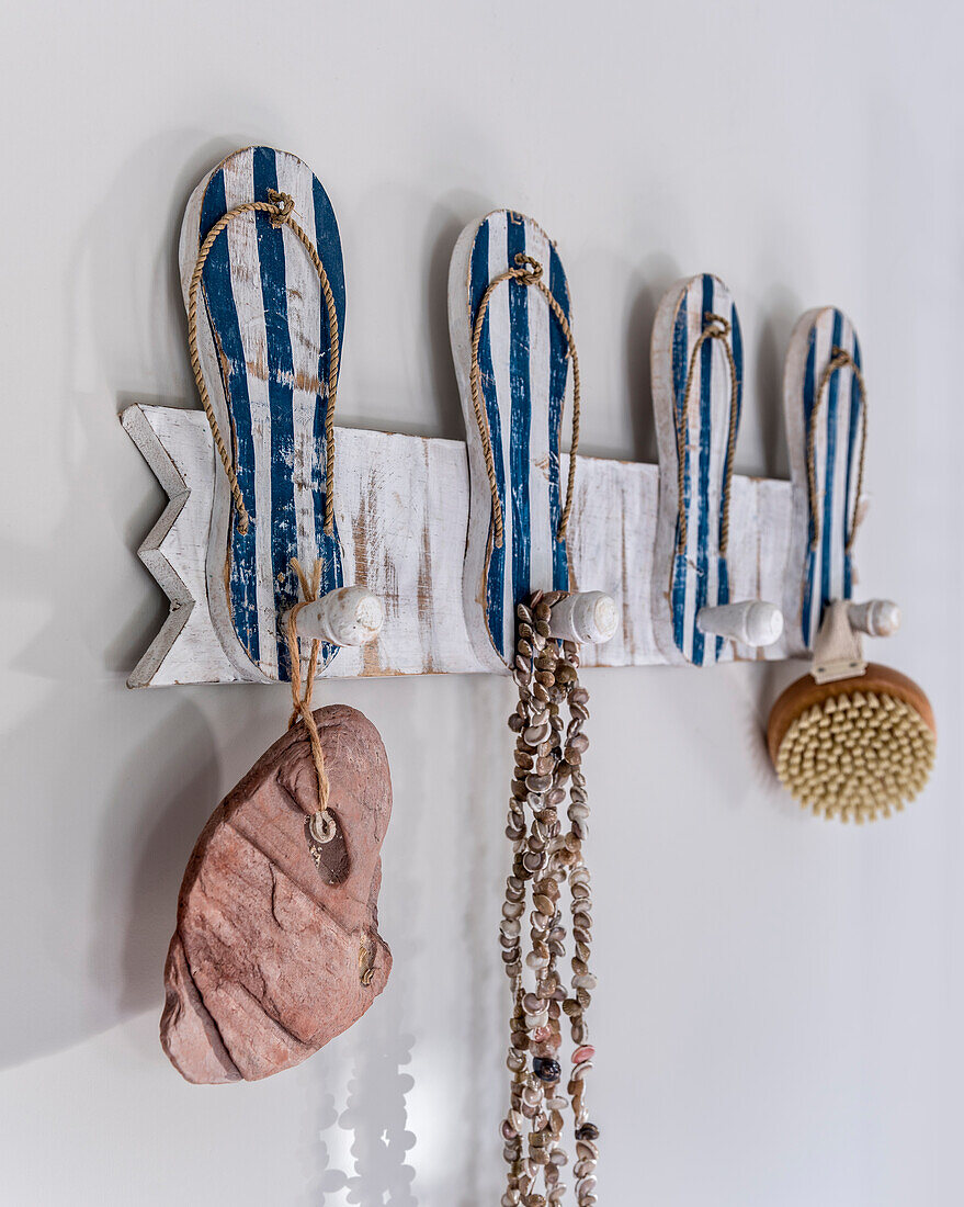 Shell necklace, body brush and stone on wall coat rack with flip-flops