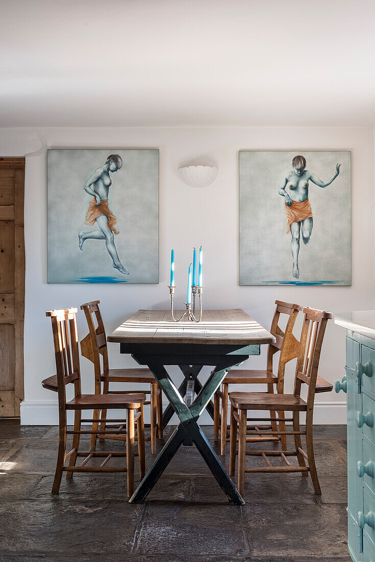 Dining table with chairs flanked by artwork in a renovated farmhouse