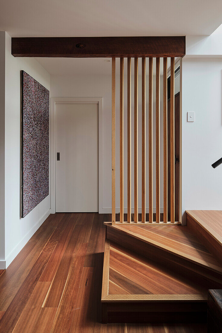 Hallway with wooden floor, staircase across the corner and room divider made of wooden slats