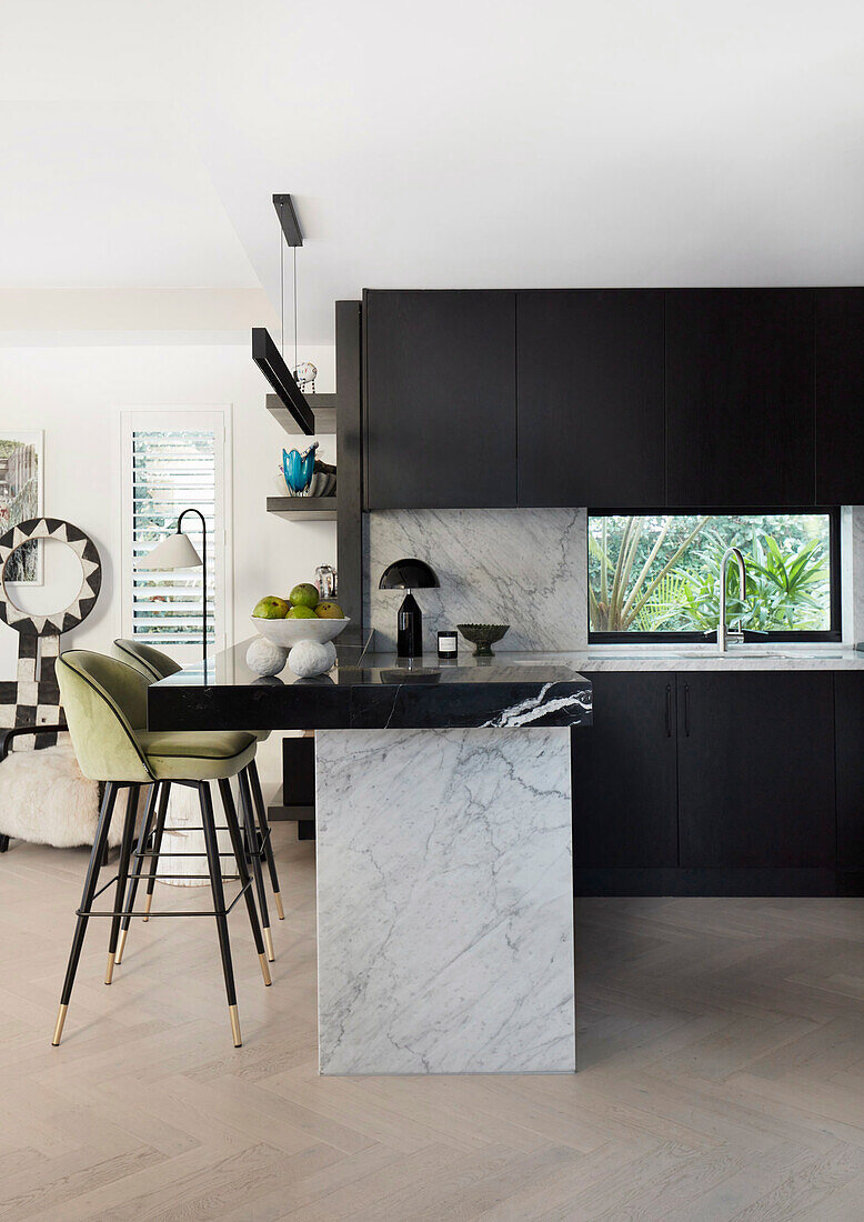Designer kitchen with black cabinet fronts and marble elements, bar stools with green upholstery