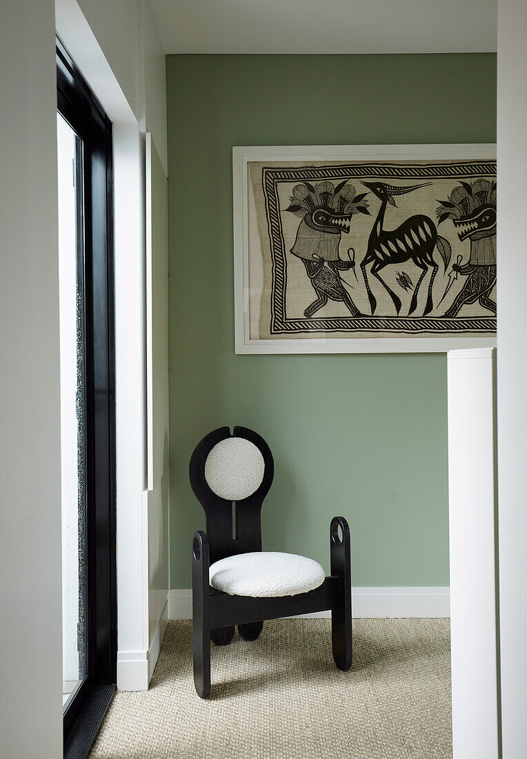 Designer chair above vintage artwork in a corner of a room with green wall