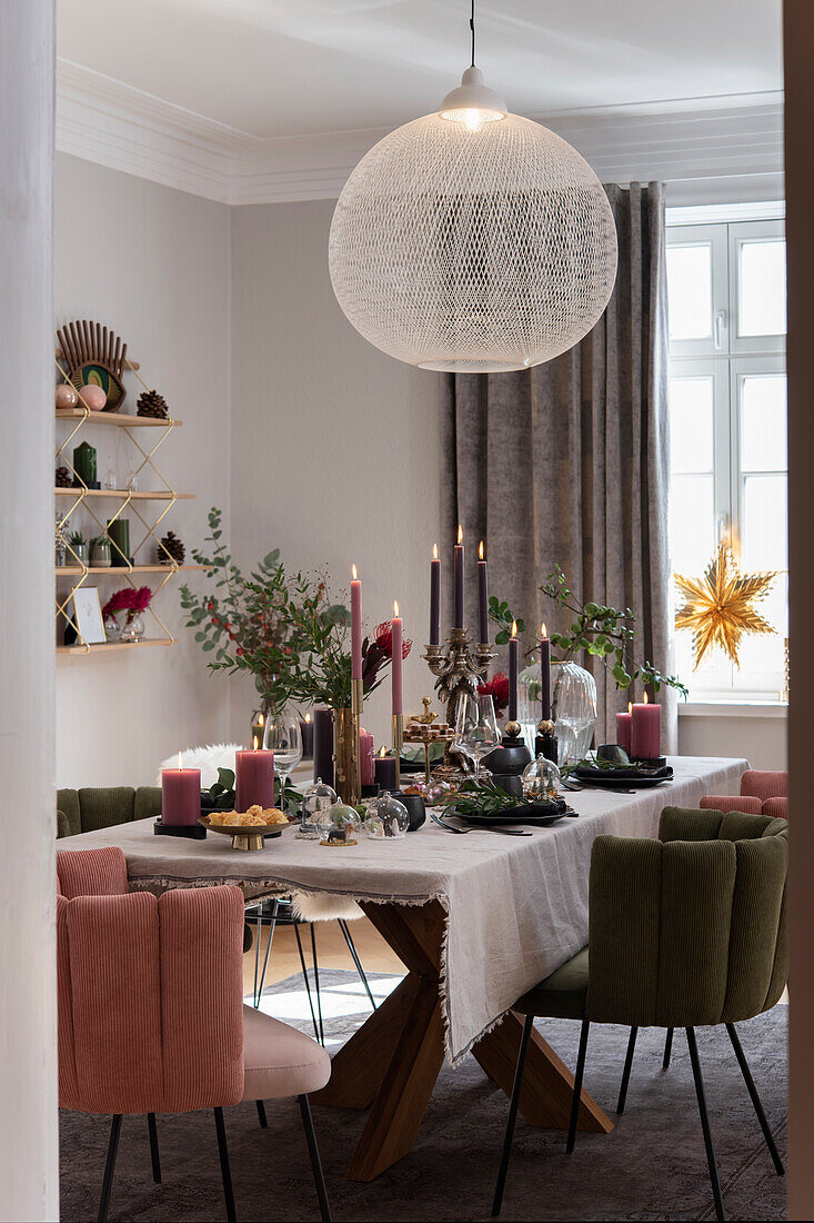 Festively laid Christmas table with candles, velvet upholstered chairs around the table